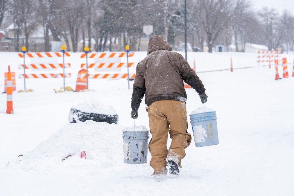 Um homem carrega baldes de neve no estacionamento da oficina de pneus onde trabalha durante a tempestade de inverno Fern, em Oklahoma City, Oklahoma, EUA, em 24 de janeiro de 2026.