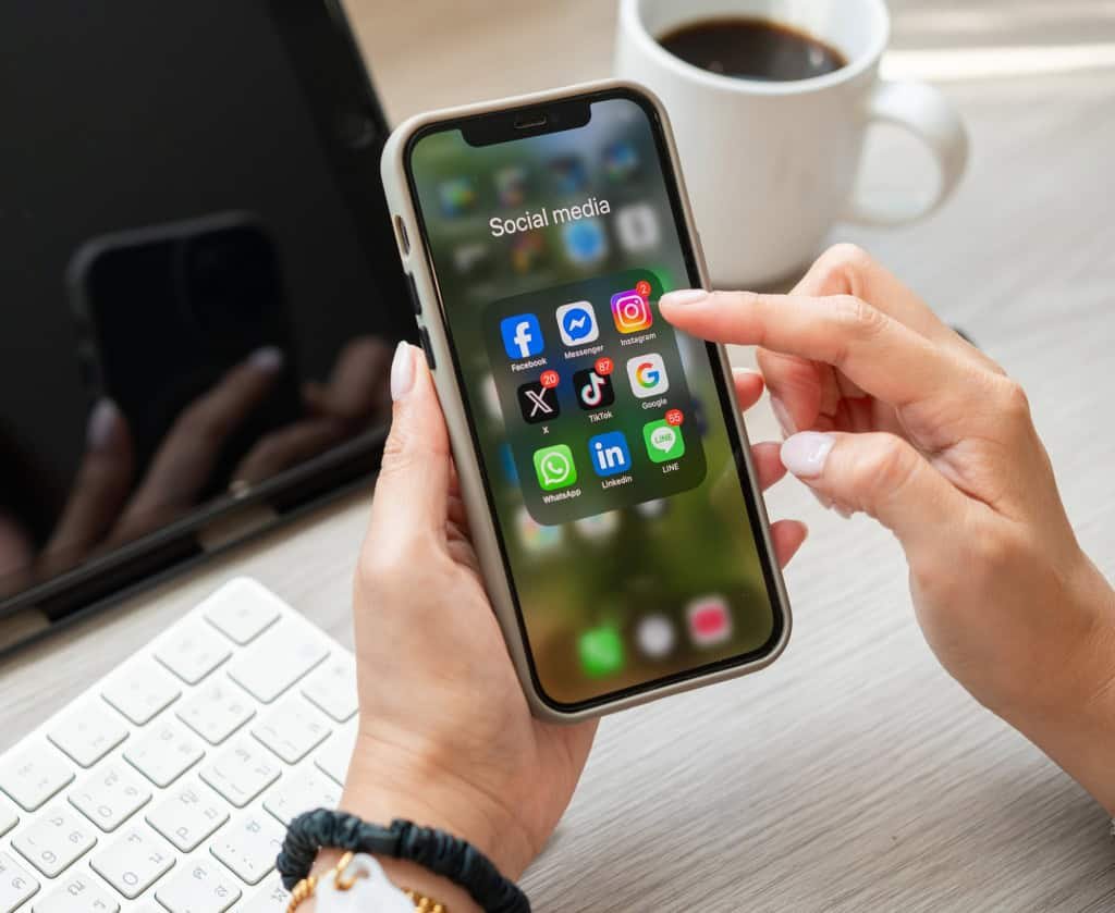 Pessoa segurando um smartphone com aplicativos de redes sociais, ilustrando o uso de plataformas que utilizam algoritmos para recomendar conteúdos.